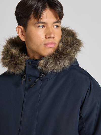 Männermodel trägt Bomberjacke mit Label-Patch Modell 'Everest' von Superdry in Dunkelblau mit Kunstfellkapuze, Nahaufnahme Oberkörper. Regular Fit, Reiß- und Druckknopfverschluss, Pattentaschen, Rückenlänge 71 cm, Schulterbreite 50 cm, Brustweite 65 cm, Ärmellänge 70 cm.