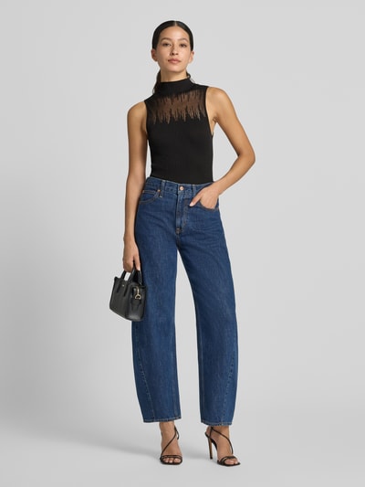 Frauenmodel trägt Slim Fit Top mit Mock Neck Modell 'Sieffy' von HUGO in Schwarz mit Mesh-Details, kombiniert mit blauen Jeans, Ganzkörperansicht von vorne. Damen Top von HUGO