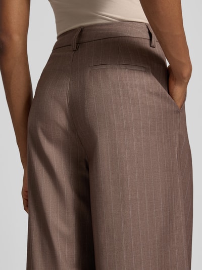 Frauenmodel trägt Wide Fit Hose mit Viskose-Anteil Modell 'Fee' von GUIDO MARIA KRETSCHMER WOMAN, braun mit Nadelstreifen, Detailaufnahme Rückansicht. Elastischer Material-Mix, Bundfalten und Gesäßtasche sichtbar.