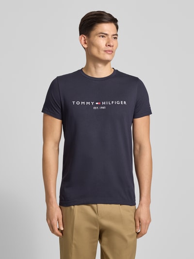 Männermodel trägt T-Shirt aus Bio-Baumwolle von Tommy Hilfiger in Dunkelblau mit weißer Logo-Stickerei, Gerader-Schnitt, Rundhalsausschnitt, Ganzkörperansicht von vorne.
