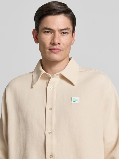 Männermodel trägt Regular Fit Freizeithemd mit Label-Patch von American Vintage in Beige, Reine Baumwolle, Kentkragen, Knopfleiste, Nahaufnahme Oberkörper. Rückenlänge 77 cm, Schulterbreite 50 cm, Ärmellänge 66 cm, Größe M/L.