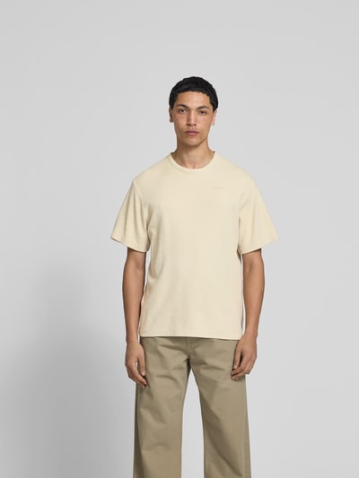 Männermodel trägt Relaxed Fit T-Shirt mit Strukturmuster von Forét in Beige, Reine Baumwolle, Logo-Stitching, Rundhalsausschnitt, Rückenlänge bei Größe M: 69 cm, Ganzkörperansicht von vorne.