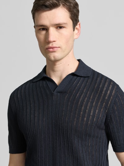 Męski model nosi Slim Fit Poloshirt aus Baumwoll-Leinen-Mix von Profuomo, mieszanka bawełny i lnu, krój slim fit, dekolt w serek, rękaw o dł. 1/2, długość tyłu w rozmiarze M: 69 cm, ciemnogranatowy, pionowe prążki, tekstura dzianiny, widoczne prześwity, Nahaufnahme górnej części ciała.