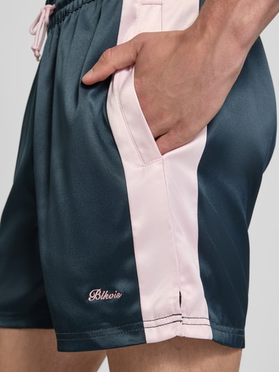 Männermodel trägt Shorts aus Satin mit Label-Stitching und elastischem Bund von BLKVIS in Dunkelblau und Rosa, Nahaufnahme Oberschenkel, Herren Shorts, Regular-Fit, Label-Stitching, Bundweite bei Größe M 42 cm, Innenbeinlänge 14 cm, Tunnelzug