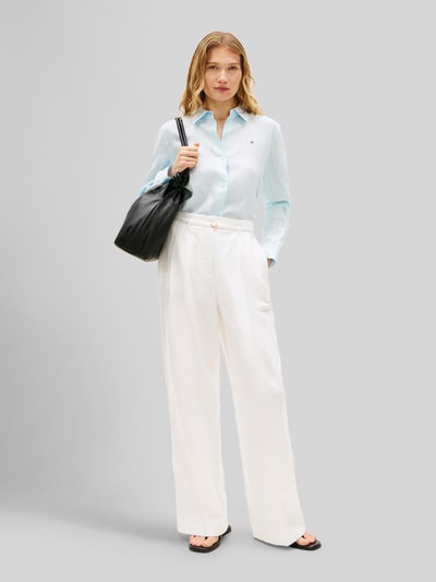 Frauenmodel trägt Relaxed Fit Langarmbluse aus reinem Leinen von Tommy Hilfiger, Optik: Unifarben, Passform: Relaxed-Fit, Hemdkragen, Logo-Stitching, Verschluss: Knopfleiste, Ärmelform: Langarm, Manschette, Rumpfabschluss: Abgerundet, Materialverarbeitung: Flammgarn, Material: Leinen, hellblaue Farbe, strukturierte Oberfläche, kombiniert mit weißer Hose, Ganzkörperansicht von vorne.