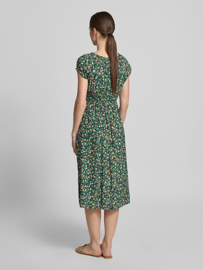 Kobiece model prezentuje Midikleid aus Viskose mit Smok-Details od Apricot, zielony z kwiatowym wzorem, dopasowany krój, długość do łydek, okrągły dekolt z falbankami, rękawy z falbankami, talia z marszczeniem, długość tyłu w rozmiarze S: 105 cm, szerokość w rozmiarze S: 40 cm, widok całej sylwetki z tyłu.
