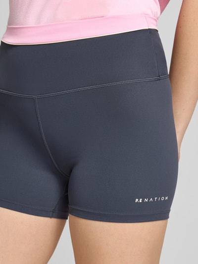 Frauenmodel trägt Slim Fit Shorts mit Logo-Print Modell 'Reflect' von P.E Nation im Elastischer-Material-Mix in Dunkelgrau, Nahaufnahme Oberschenkel.