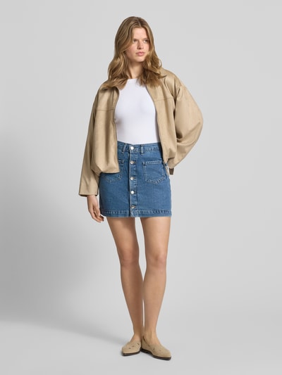 Frauenmodel trägt schmalen Jeansrock aus reiner Baumwolle Modell 'AMAZING' von Only mit Denim-Optik, Mini-Länge, Kontrastnaht, Gürtelschlaufen, einreihiger Knopfleiste und aufgesetzten Eingrifftaschen, Ganzkörperansicht von vorne.