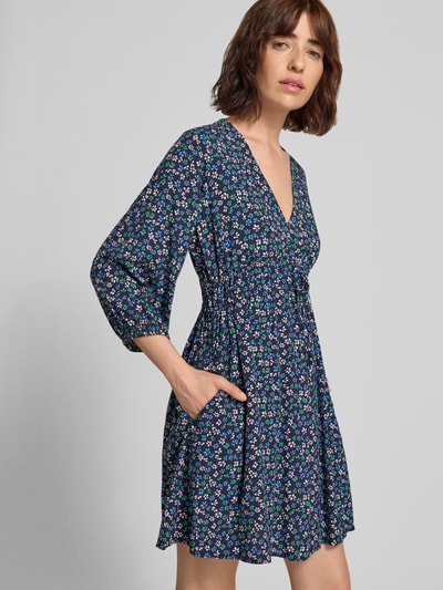 Frauenmodel trägt Minikleid aus reiner Viskose mit floralem Allover-Print von GAP, tailliert, V-Ausschnitt, 3/4-Arm, Ganzkörperansicht von vorne.