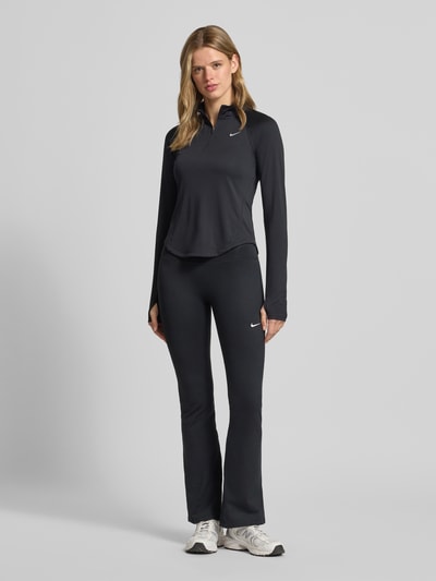 Frauenmodel trägt schwarzes Funktionsshirt mit Reißverschluss und Logo Modell 'Tempo' von NIKE TRAINING, Slim-Fit, Stehkragen, Rückenlänge 58 cm, Ganzkörperansicht von vorne.