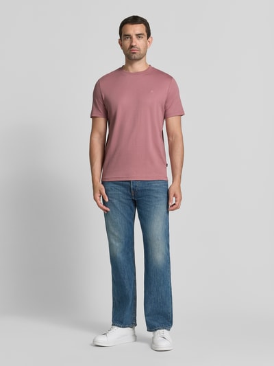 Mężczyznamodel nosi T-Shirt mit Rundhalsausschnitt und Logo-Stitching od JOOP! COLLECTION z bawełny, krój regular fit, różowy, okrągły dekolt, wyhaftowane logo, długość tyłu w rozmiarze M: 68 cm, widok całej sylwetki z przodu.