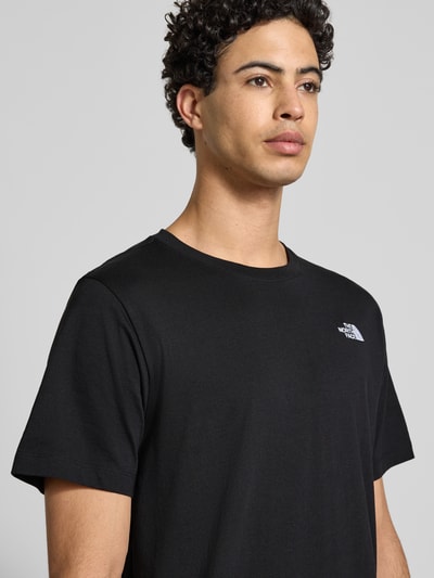 Männermodel trägt Regular Fit T-Shirt aus Baumwoll-Mix Modell 'EVOLUTION' von The North Face in Schwarz mit Label-Detail, Nahaufnahme Oberkörper.