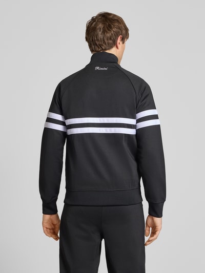 Męski model nosi bluza rozpinana z mieszanki bawełny model 'RIMINI' od Ellesse, czarna z białymi paskami, prosty krój, stójka, długość tyłu 71 cm, długość rękawa 43 cm, detale z logo, elastyczne wykończenia, całkowity widok z tyłu.