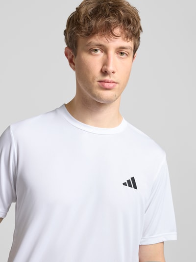 Mannelijk model draagt T-shirt met labelprint van adidas Training in wit, regular fit, ronde hals, ruglengte maat M 72 cm, nahaufnahme bovenlichaam.