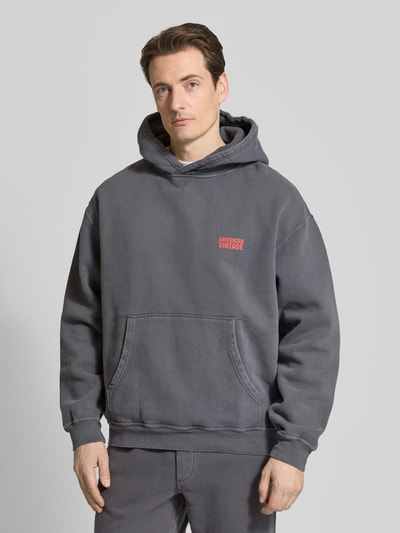 Männermodel trägt Hoodie aus Baumwolle Modell 'PLIZZY' von American Vintage in Grau mit Känguru-Tasche, Label-Detail, Lockerer-Schnitt, Nahaufnahme Oberkörper.