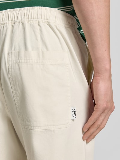 Mężczyznamodel nosi spodnie Regular Fit Hose mit elastischem Bund Modell 'Lax' z bawełny od Wood Wood, kremowy kolor, tył z detalem kieszeni, długość wewnętrzna nogawki w rozmiarze M: 78 cm, szerokość w rozmiarze M: 40 cm, materiał o gładkiej fakturze, detalaufnahme tylnej kieszeni.