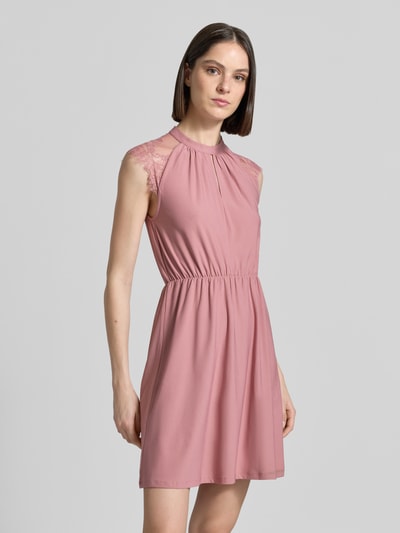 Frauenmodel trägt Tailliertes Freizeitkleid mit Spitzenbesatz Modell 'MILLA' von Vero Moda in Altrosa, unifarben, Stretchstoff, Mini-Länge, tailliert, hochgeschlossen, kurzer Knopfleiste, kurze Ärmel, Ganzkörperansicht von vorne.