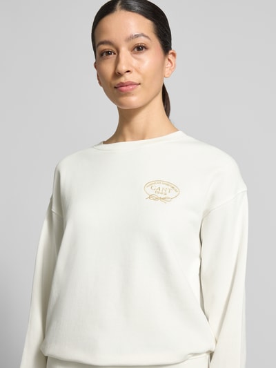 Frauenmodel trägt Sweatshirt mit Label-Stitching und Rundhalsausschnitt von Gant aus reiner Baumwolle in Offwhite, Nahaufnahme Oberkörper.
