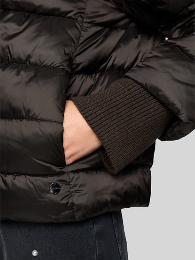 Frauenmodel trägt Steppjacke mit Stehkragen und Label-Detail von Marc Cain in Dunkelbraun, glatte und gesteppte Textur, Nahaufnahme Oberkörper. Damen Steppjacke, Regular Fit, Eingrifftaschen, Schulterbreite 41 cm, Brustweite 55 cm, Ärmellänge 73 cm, Rückenlänge 56 cm.