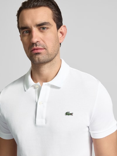 Männermodel trägt Slim Fit Poloshirt aus reiner Baumwolle von Lacoste, Optik: Unifarben, Logo-Stitching, Piqué-Struktur, Nahaufnahme Oberkörper.