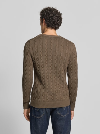 Männermodel trägt Regular Fit Pullover aus reiner Baumwolle von GANT in Braun mit Zopfmuster, glatter Textur, Ganzkörperansicht Rückansicht.