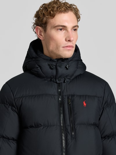 Męski model nosi czarną kurtkę puchową Regular Fit Daunenjacke mit Logo-Stitching von Polo Ralph Lauren, gładka tekstura, widoczne wyhaftowane logo, zbliżenie na górną część ciała, kontekst: Herren Daunenjacke von Polo Ralph Lauren.