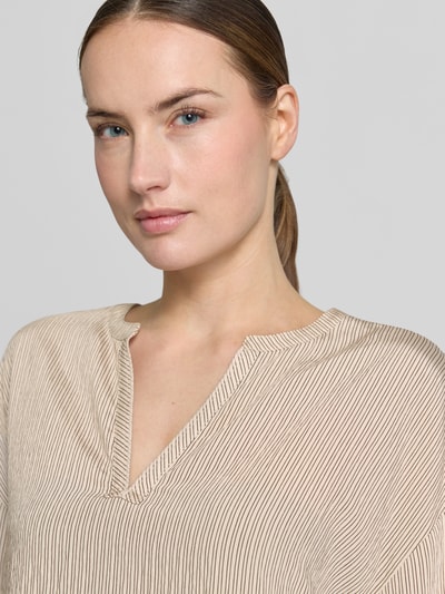 Modelka kobieca nosi Bluse aus Viskose-Mix mit Kimonoärmeln od comma, beżowa, prążkowana tekstura, tunikowy kołnierz, luźny krój, długość tyłu 63 cm, długość rękawa 53 cm, widok z przodu, zbliżenie na górną część ciała.