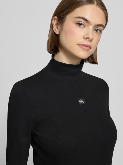 Vrouwenmodel draagt Turtleneck-Pullover met Label-Detail van Calvin Klein Jeans, zwart, mix van katoen en elastaan, nauwsluitend model, opstaande kraag, labeldetail, ruglengte maat S 56 cm, Nahaufnahme bovenlichaam.
