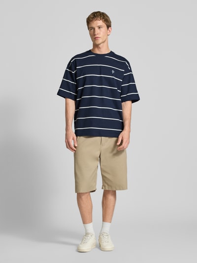 Männermodel trägt T-Shirt mit Rundhalsausschnitt und Logo-Stitching von REVIEW, gestreift in Dunkelblau, Reine Baumwolle, Loose-Fit, Ganzkörperansicht von vorne.
