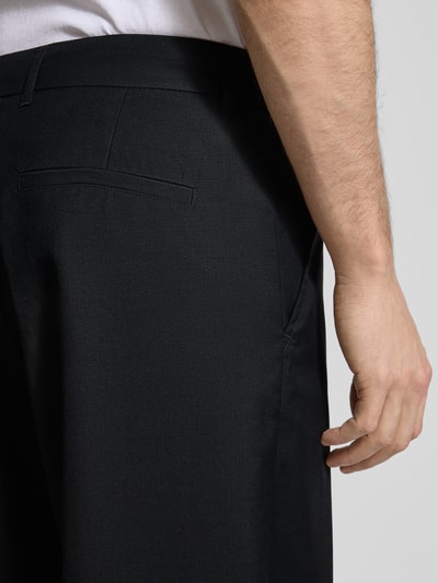 Mężczyzna nosi Hose aus Woll-Mix Modell 'Luca' von Wood Wood czarny, krój regular fit, z kantami i kieszeniami, zbliżenie na tył, kontekst produktu: spodnie męskie, wełniany miks, szerokość w rozmiarze M: 43 cm, długość wewnętrzna nogawki w rozmiarze M: 79 cm.