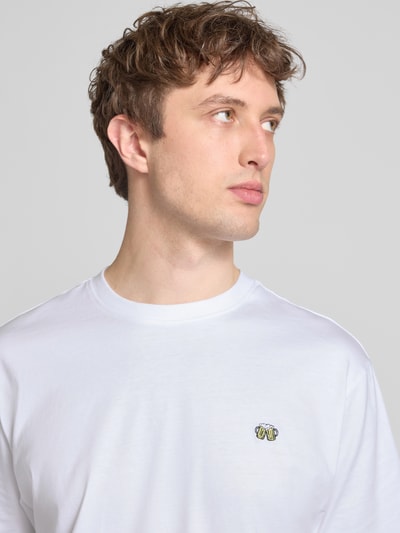 Männermodel trägt Relaxed Fit T-Shirt aus reiner Baumwolle Modell 'FRED' von Only & Sons, weiß, Rundhals, Label Patch, Motiv-Stitching, Nahaufnahme Oberkörper.