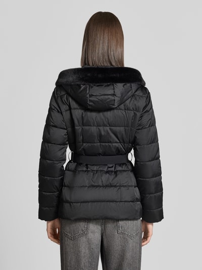 Modelka prezentuje kurtkę 'Jacke in Stepp-Optik' od monari, czarny kolor, z efektem pikowania, krój taliowany, kaptur z obszyciem sztucznym futrem, ocieplona stójka, zamek błyskawiczny dwustronny, Długość tyłu w rozmiarze 36: 68 cm, Szerokość ramion w rozmiarze 36: 46 cm, Szerokość w rozmiarze 36: 50 cm, Długość rękawów w rozmiarze 36: 63 cm, widok całej sylwetki od tyłu.