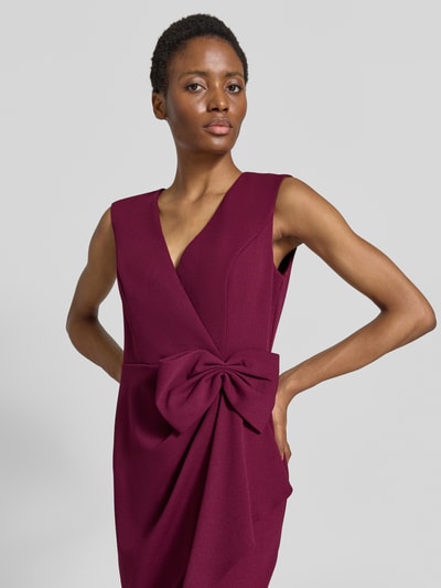 Frauenmodel trägt Knielanges Kleid mit Zierschleife von Adrianna Papell in Weinrot, ärmellos, V-Ausschnitt, tailliert, Nahaufnahme Oberkörper. Elastischer Material-Mix mit Wickel-Optik und Raffungen, Zierschleife auf Taillenhöhe, schlichte Textur.