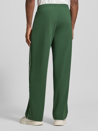 Männermodel trägt grüne Trackpants aus Viskose-Mix von EA7 Emporio Armani mit Galonstreifen und Ziernähten, Ganzkörperansicht Rückansicht.