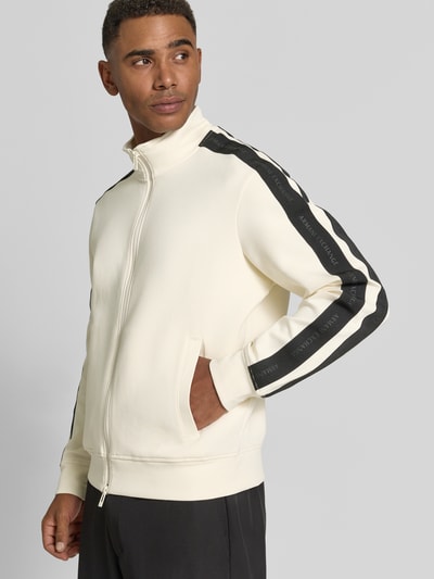 Männermodel trägt Regular Fit Sweatjacke aus Baumwoll-Mix Modell 'Felpa' von Armani Exchange, creme mit schwarzen Streifen, Ganzkörperansicht von vorne, Herren Sweatjacke, elastischer Baumwoll-Mix, Stehkragen, Zweiwege-Reißverschluss, Eingrifftaschen, elastische Abschlüsse