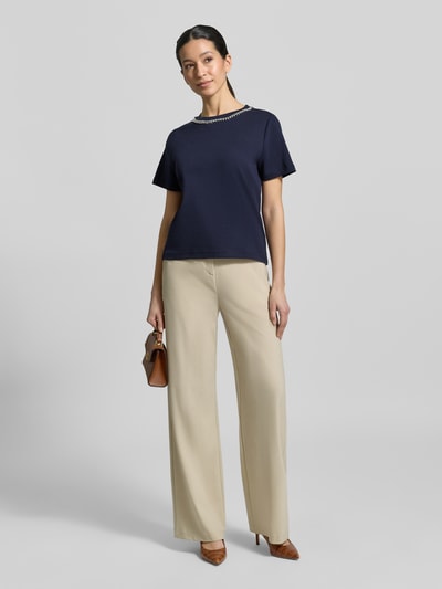 Modelka kobieca ma na sobie T-Shirt mit Perlen und Ziersteinbesatz od Christian Berg Woman, bawełna, krój regular fit, okrągły dekolt, perły, ozdobne kamienie, długość pleców w rozmiarze S: 53 cm, granat i beż, widok całej sylwetki z przodu.