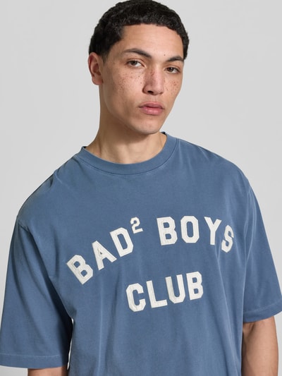 Männermodel trägt Loose Fit T-Shirt mit Rundhalsausschnitt von Dsquared2, Statement-Print, Used-Look, blau, Nahaufnahme Oberkörper.