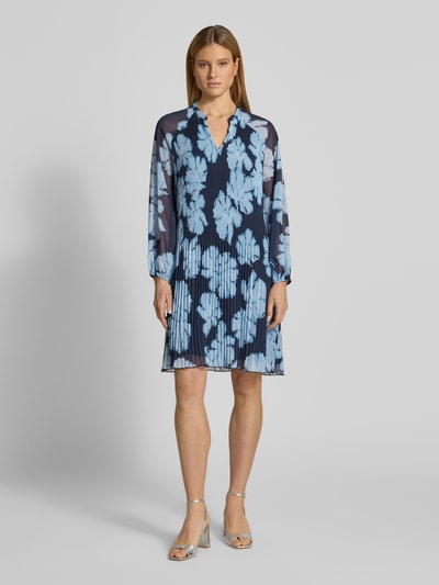 Frauenmodel trägt Knielanges Cocktailkleid mit Plisseefalten und Tunika-Ausschnitt von Christian Berg Cocktail, blau mit Blumenmuster, Chiffon, tailliert, knieumspielend, Ballonärmel, blickdichtes Unterkleid, Ganzkörperansicht von vorne.