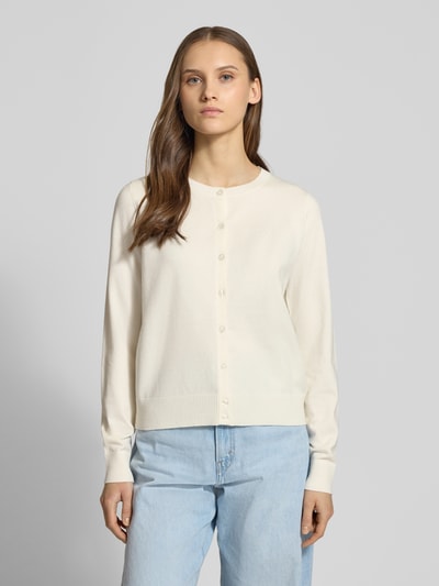 Modelka nosi Strick-Cardigan aus Viskose-Mix mit langen Ärmeln od Review, kolor kremowy, krój regular fit, długie rękawy, prążkowane ściągacze, zapięcie na guziki, haftowane logo, długość tyłu 53 cm, długość rękawa 63 cm, widok całej sylwetki z przodu.