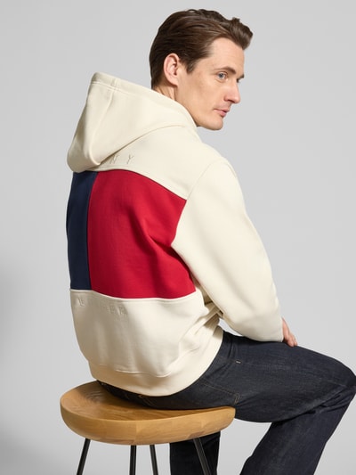 Männermodel trägt Regular Fit Hoodie aus reiner Baumwolle von Tommy Hilfiger in Creme mit großem Farbfeld-Logo auf dem Rücken, Ganzkörperansicht Rückansicht.