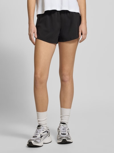 Frauenmodel trägt Regular Fit Shorts mit elastischem Bund von PUMA in Schwarz, Logo-Print, ausgestellte Passform, Nahaufnahme Oberschenkel.