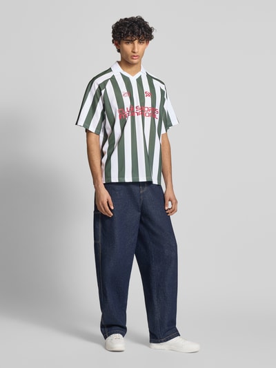 Männermodel trägt Loose Fit Poloshirt mit Motiv-Print Modell 'ZIDAN' von Only & Sons, grün-weiß gestreift, Piqué, Ganzkörperansicht von vorne.