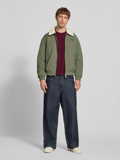 Männermodel trägt Slim Fit Pullover aus reiner Baumwolle von Tommy Jeans in Unifarben, Struktur-Strickoptik, Ganzkörperansicht von vorne.