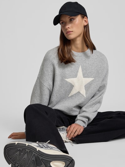 Vrouwenmodel draagt Regular Fit Pullover in tricotlook van REVIEW, materiaalmix met stretch, grijs met witte ster, lange mouw, zittend, close-up bovenlichaam.