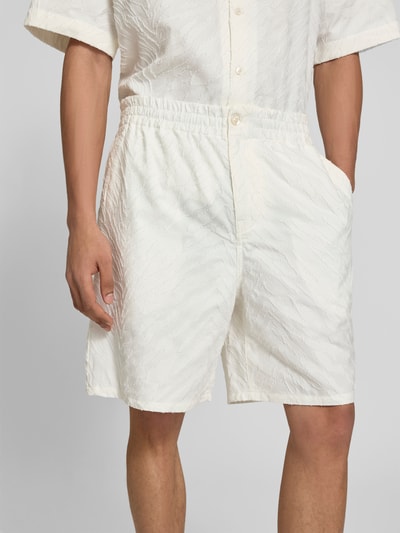 Männermodel trägt Shorts mit Strukturmuster von Kenzo, biała bawełna, krój straight fit, kieszenie z tyłu, zapięcie na guzik i zamek, długość wewnętrzna nogawki w rozmiarze M: 19 cm, szerokość w rozmiarze M: 44 cm, zbliżenie na przednią część ciała