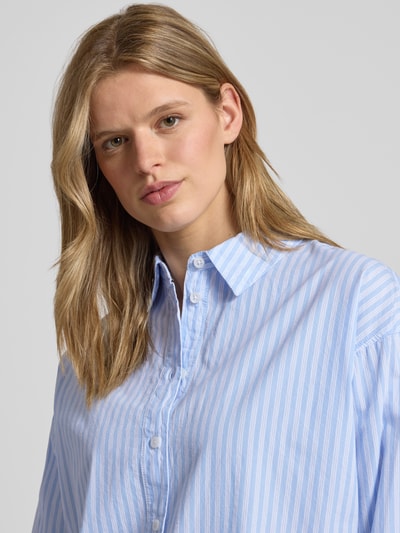 Vrouwenmodel draagt Basic Hemdbluse aus reiner Baumwolle van REVIEW in blauw-wit gestreept, relaxed fit, all-over look, overhemdkraag, knoopsluiting, puur katoen, ruglengte maat S 65 cm, mouwlengte maat S 56 cm, close-up bovenlichaam.