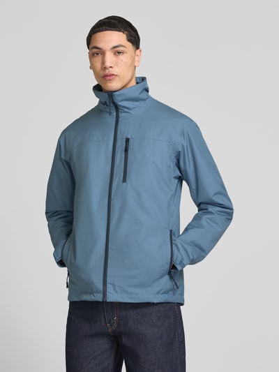 Męskimodel nosi kurtkę Midlayer Jacke mit Stehkragen Modell 'CREW' od Helly Hansen, prosty krój, stójka, niebieska, nadruk z logo, brustasza, boczne kieszenie zapinane na zamek błyskawiczny, naszywka z logo, długość tyłu w rozmiarze M: 74 cm, szerokość ramion w rozmiarze M: 49 cm, szerokość w rozmiarze M: 52 cm, długość rękawów w rozmiarze M: 68 cm, zdjęcie: całkowity widok z przodu