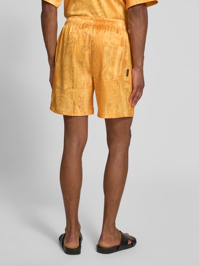 Männermodel trägt Straight Fit Shorts mit elastischem Bund Modell 'Resort' von COLUCCI, elastyczna mieszanka materiałów, szerokość w rozmiarze M 39 cm, długość wewnętrzna nogawki 16 cm, kolor pomarańczowy, wzór żakardowy, widoczne detale kieszeni, szorty męskie, Ganzkörperansicht Rückansicht.