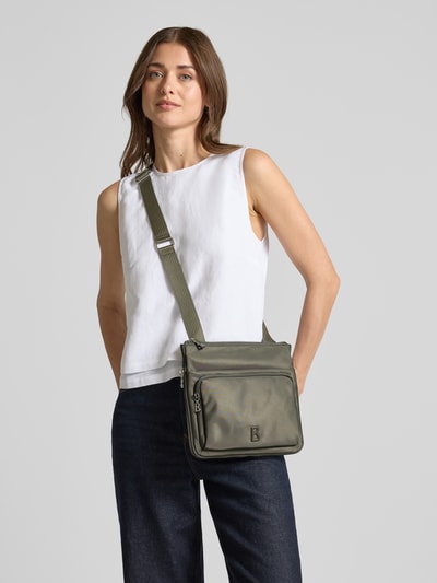 Frauenmodel trägt Handtasche mit Label-Detail Modell 'verbier play 1.0 serena' von BOGNER, schlichte Farben, glatte Textur, Ganzkörperansicht von vorne, Hauptfach mit Reißverschluss, verstellbarer Schulterriemen, Breite 25 cm, Länge 25 cm, Tiefe 4 cm, Riemenlänge 105 cm.