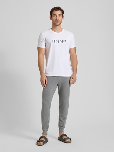 Männermodel trägt Sweatpants mit elastischem Bund und Tunnelzug von JOOP! Collection aus Baumwoll-Mix mit Stretch-Anteil, Regular-Fit, graue Farbe, Ganzkörperansicht von vorne.